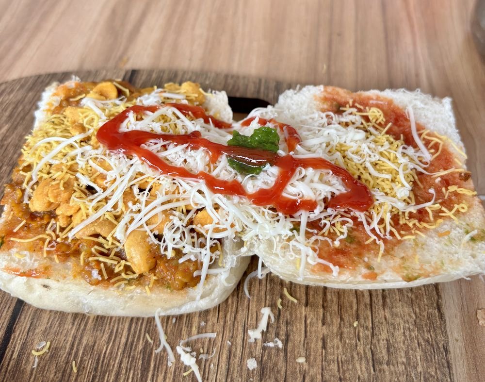 Dabeli topped with sev, peanuts, cheese and sauce