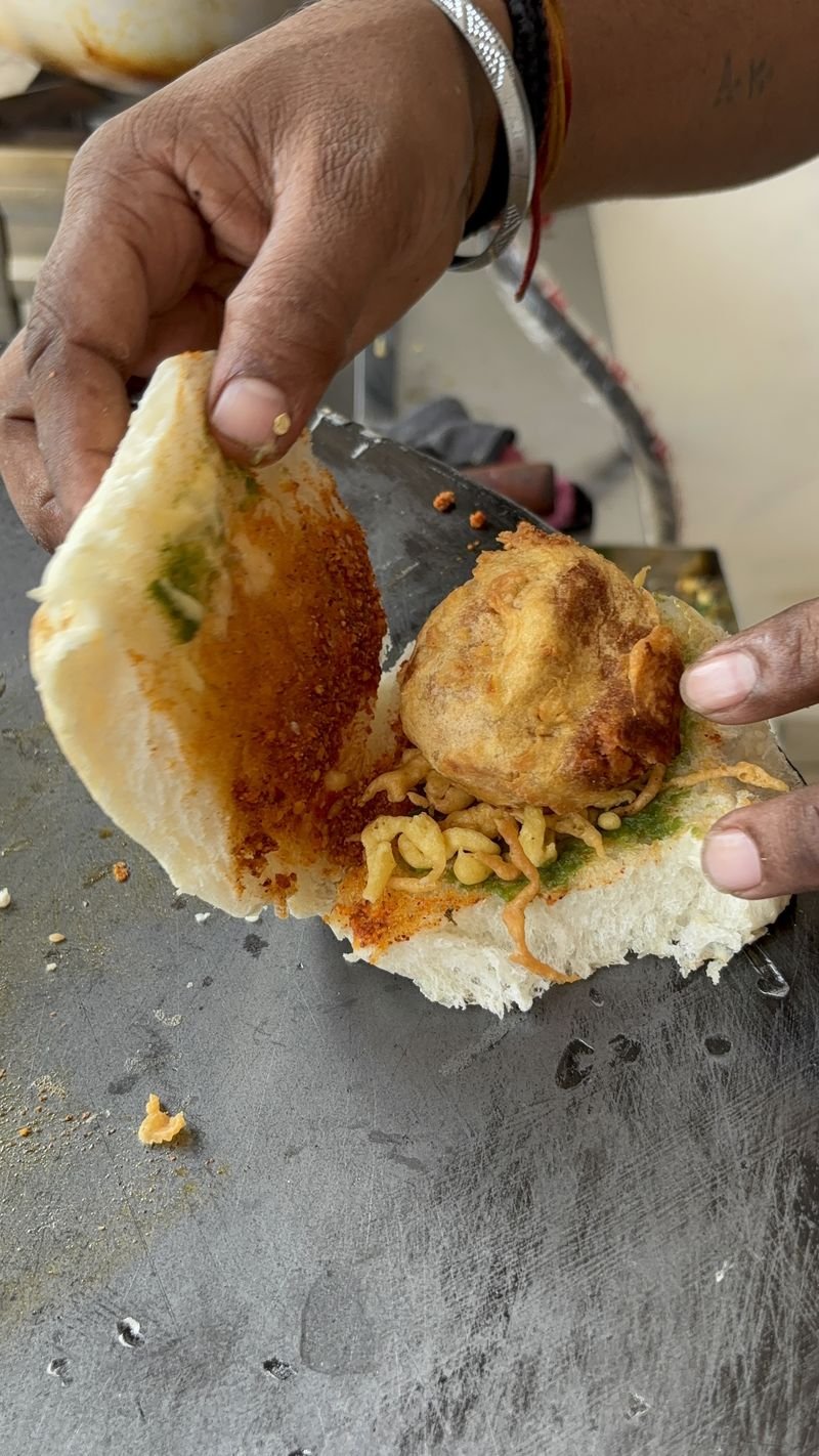Vadapav being assembled with chutneys and a fresh vada